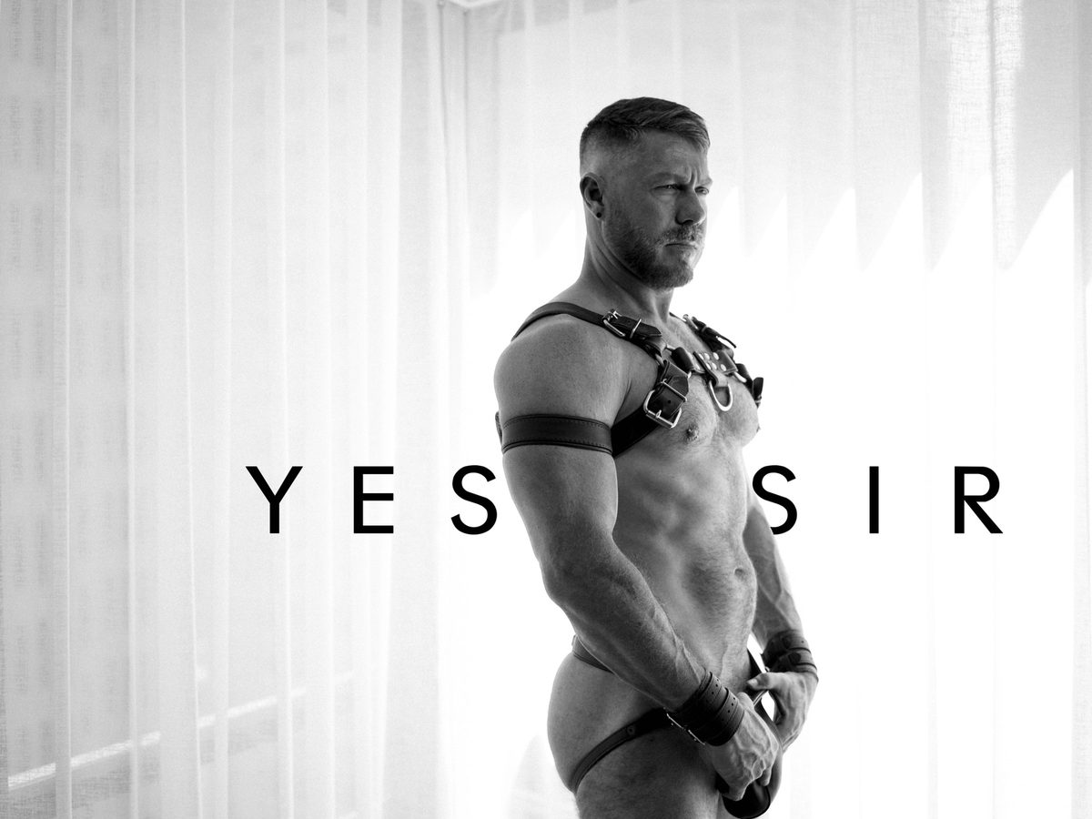 Spread 1 of 5 from Yes Sir: a bearded man in a leather harness and jockstrap stands at a curtained window; black and white.