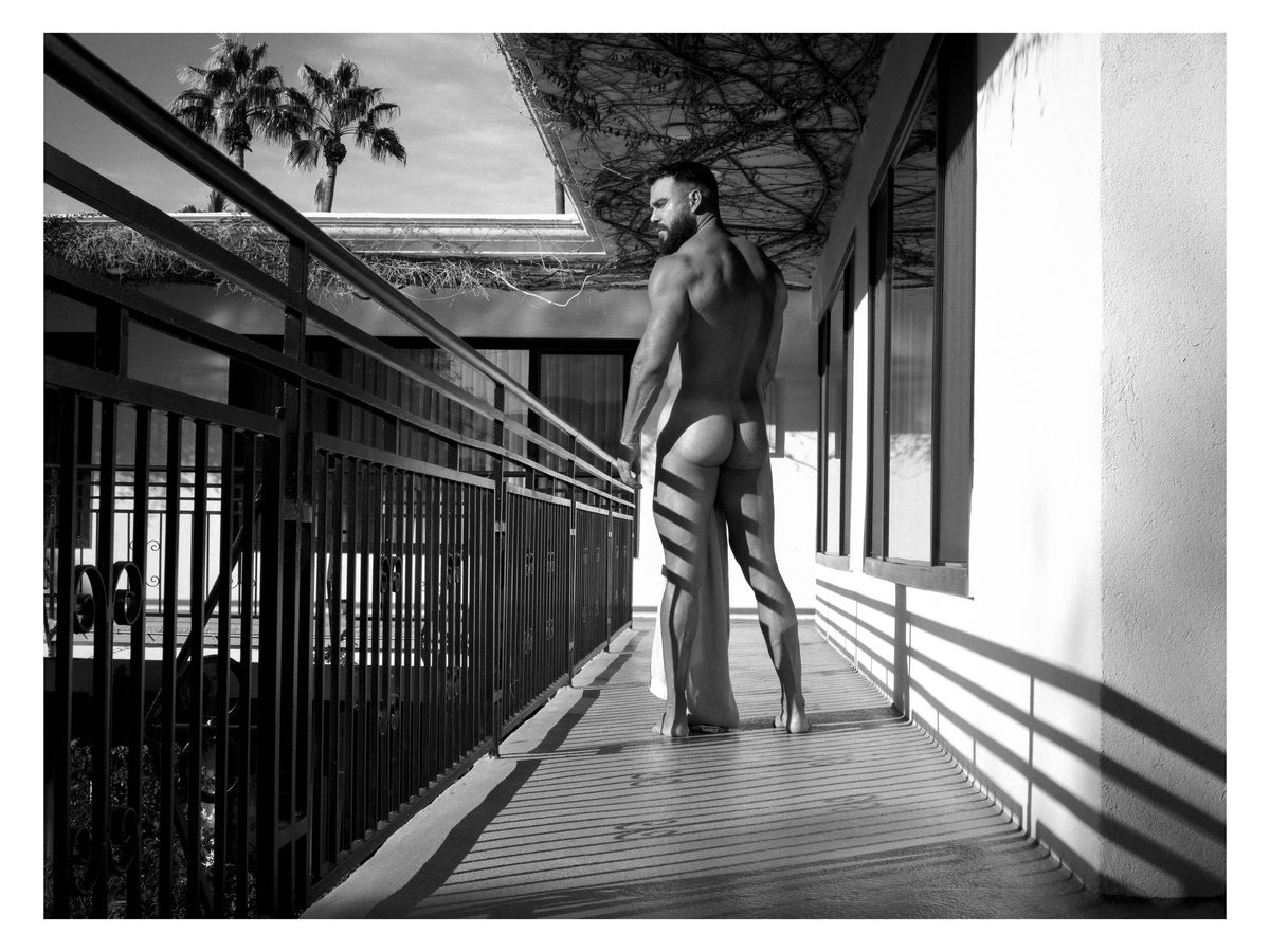 Spread 6 of 7 from Descanso: a nude man stands on a railed walkway at dusk, seen from behind, palm trees beyond; black and white.