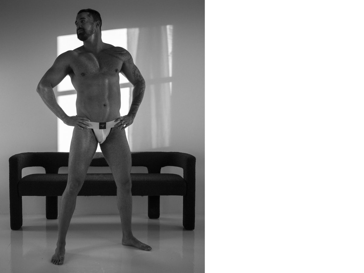 Spread 2 of 2 from Sweaty Johnson: a bearded, muscular man in a jockstrap stands with hands on his hips in a studio; black and white.