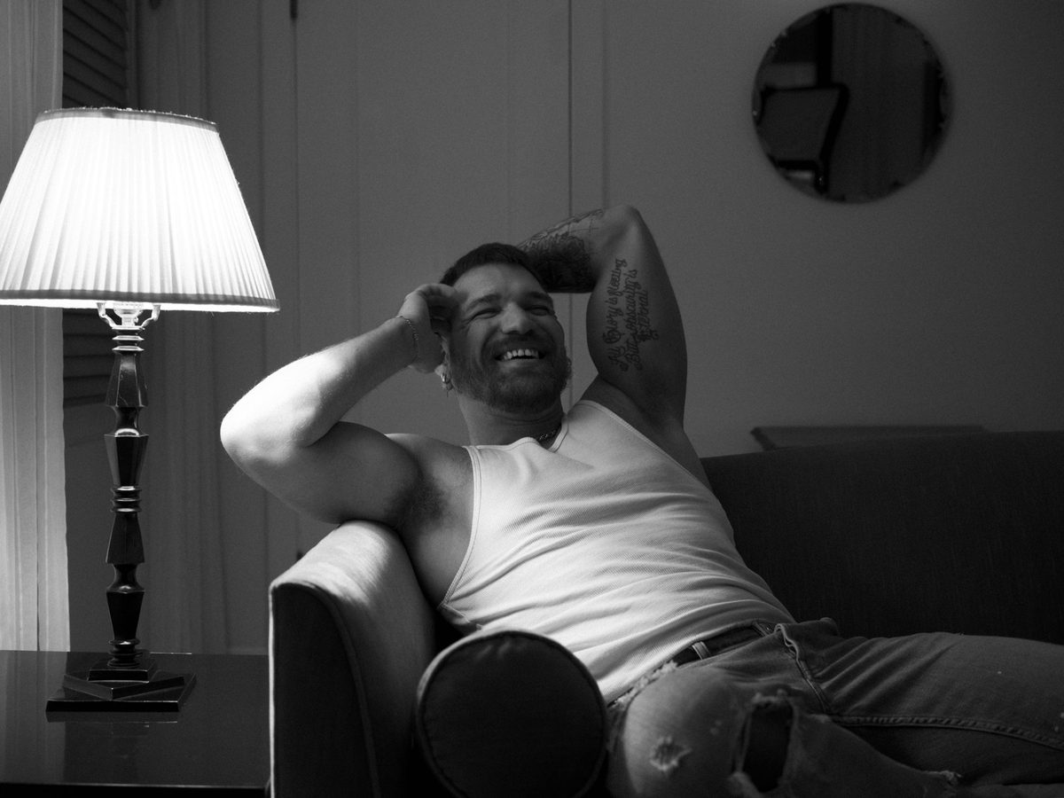 Spread 1 of 10 from Chateau Marmont: two photographs of a tattooed man in a tank top, reclining on an armchair laughing; black and white.