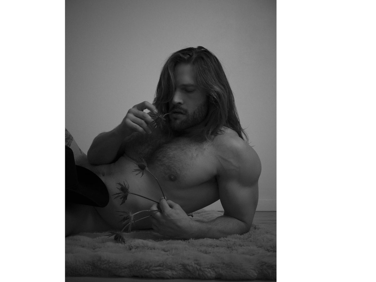 Spread 3 of 10 from Cowboy Daisy: a long-haired, bearded man reclines on a fur rug, shirtless, holding a dried flower; black and white.