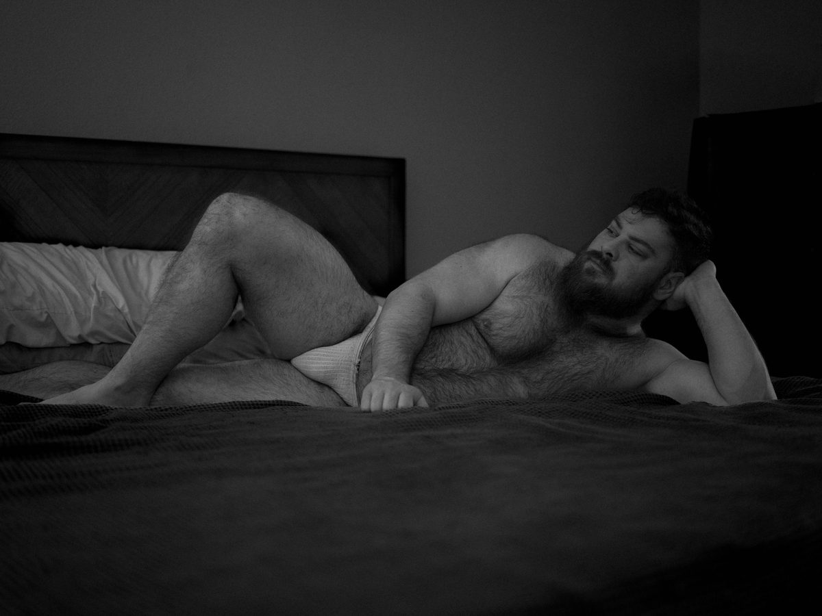 Spread 9 of 10 from Bear Bottom: a heavyset, bearded man reclines across a bed in briefs, head resting on his hand; black and white.