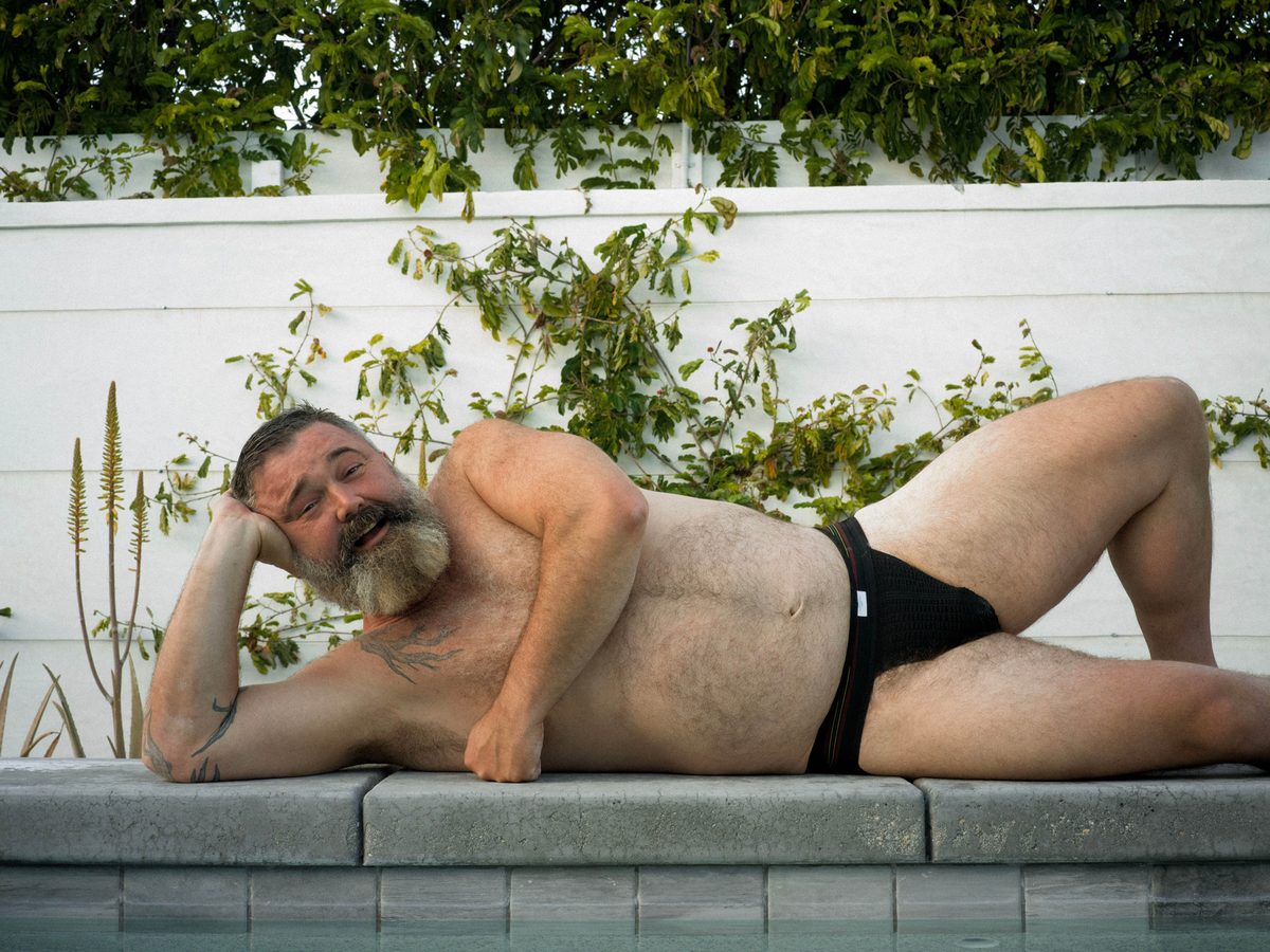 Spread 9 of 10: a bearded man in briefs reclines poolside, head resting on his hand; colour.