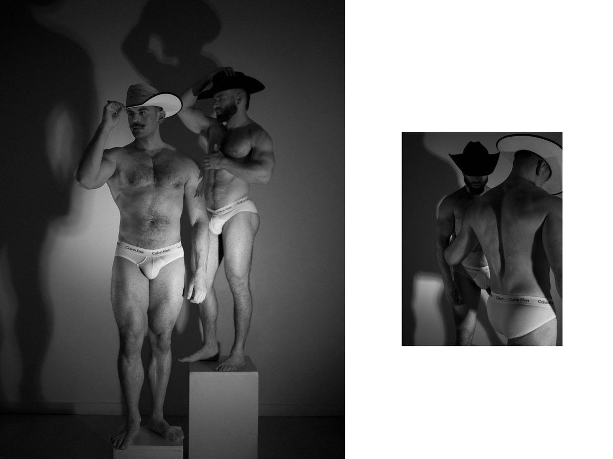 Spread 1 of 15 from Tension: two men in cowboy hats and briefs stand together on a pedestal, dramatic shadow behind them; black and white.