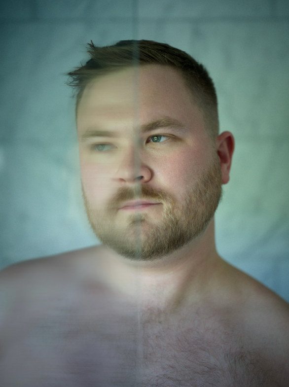 A close portrait of a man's bare shoulders and face in a two-tone colour treatment, half cool, half warm; colour.